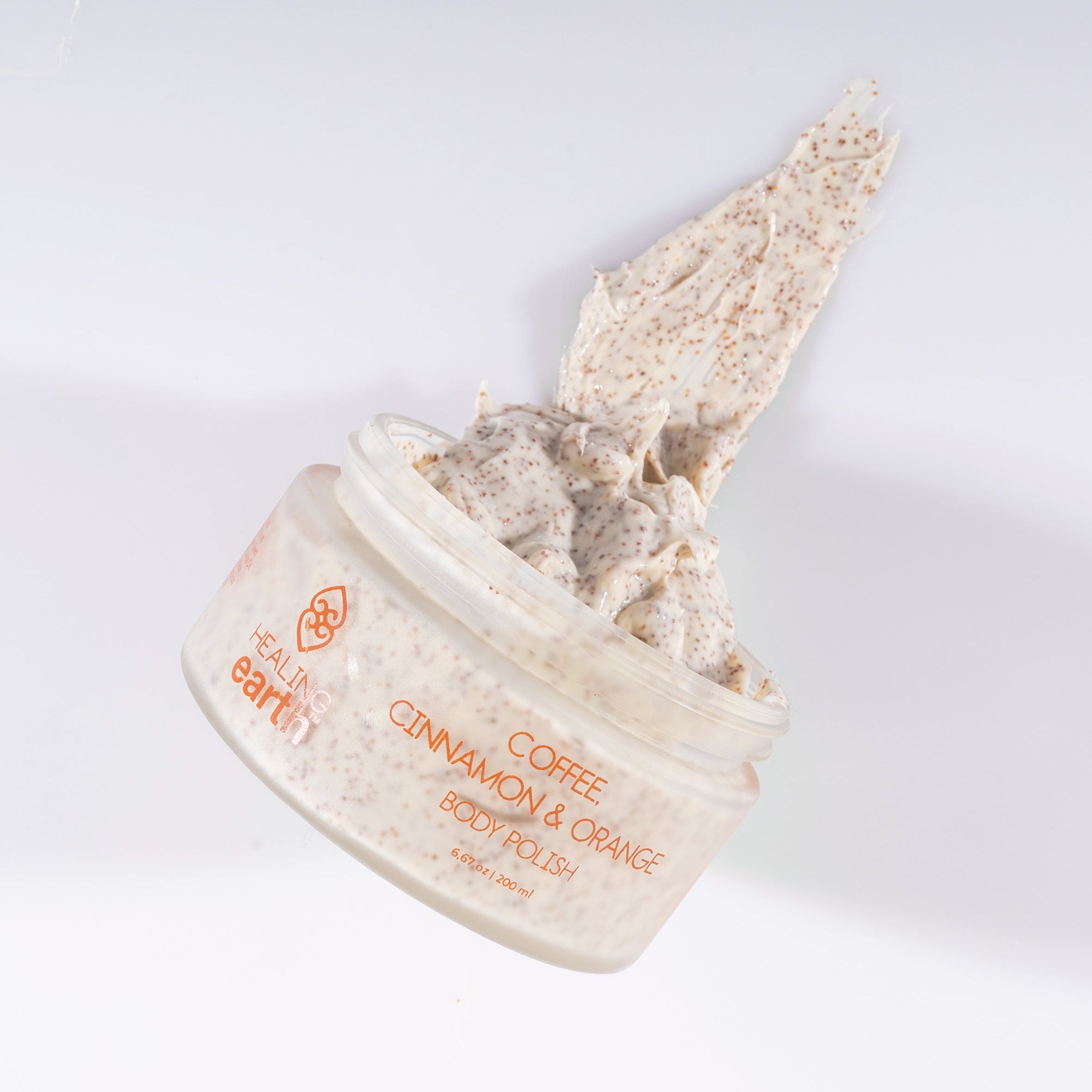 Cosmetic container with a scoop of Coffee, Cinnamon & Orange Body Polish on a white background